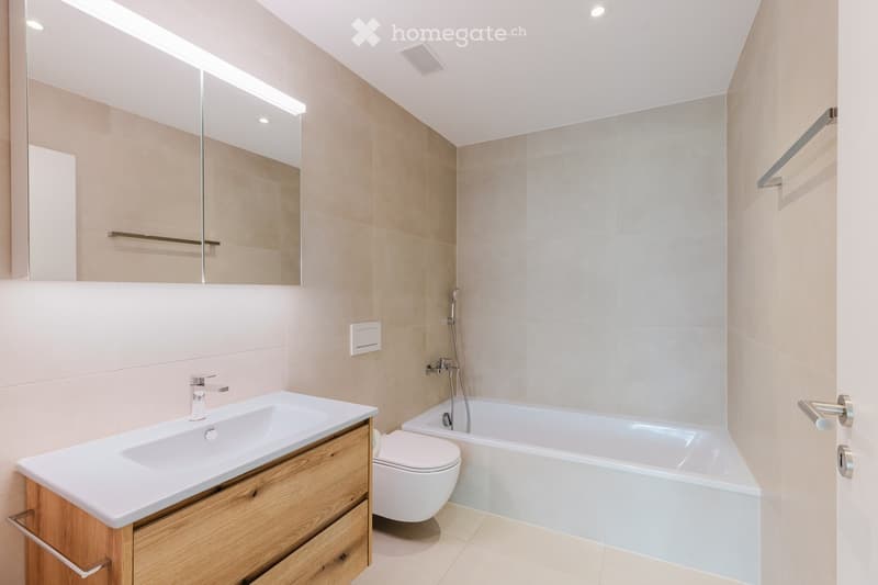 Modern bathroom with a white sink, wooden cabinet, toilet, bathtub, and large mirror with built-in lighting.