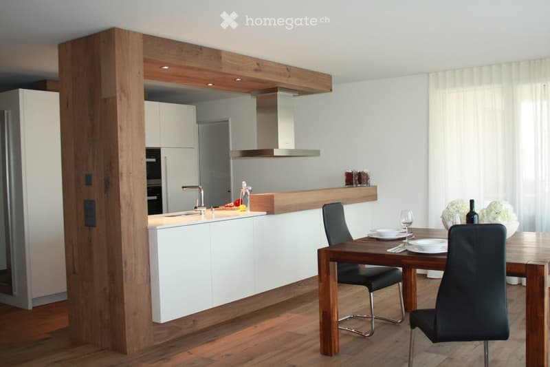 Modern kitchen with white cabinets, wooden accents, a central island, and a dining area with a wooden table and black chairs.