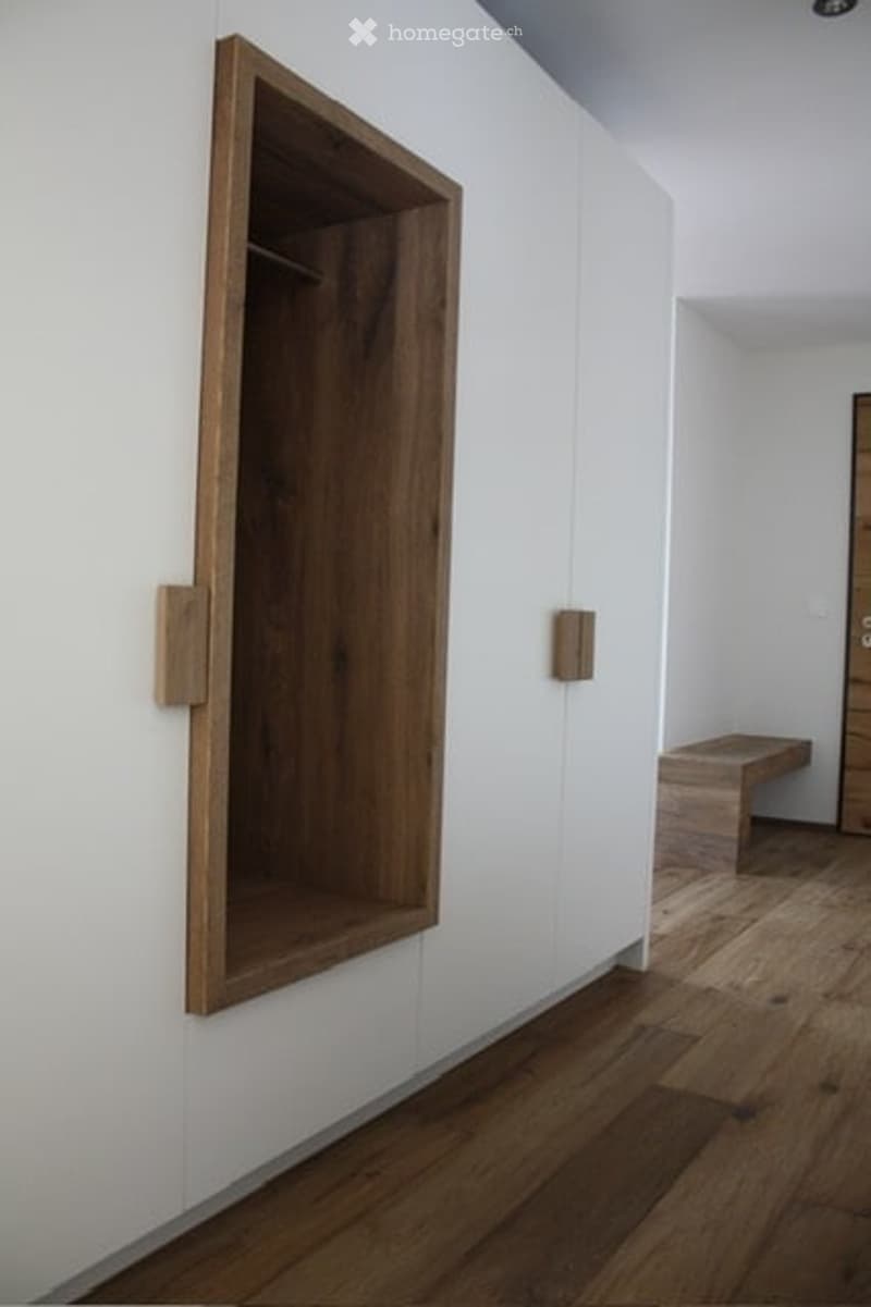 Minimalist hallway with white walls, wooden floor, built-in wooden shelf, and a small wooden bench.