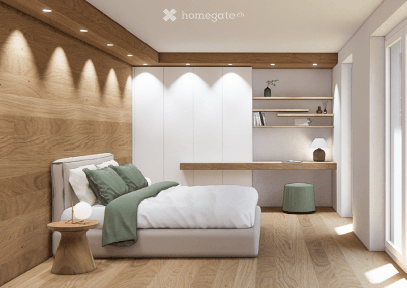 Modern bedroom with a large bed, green pillows and blanket, wooden nightstand, small round stool, built-in desk with shelves, and a small lamp on the desk.