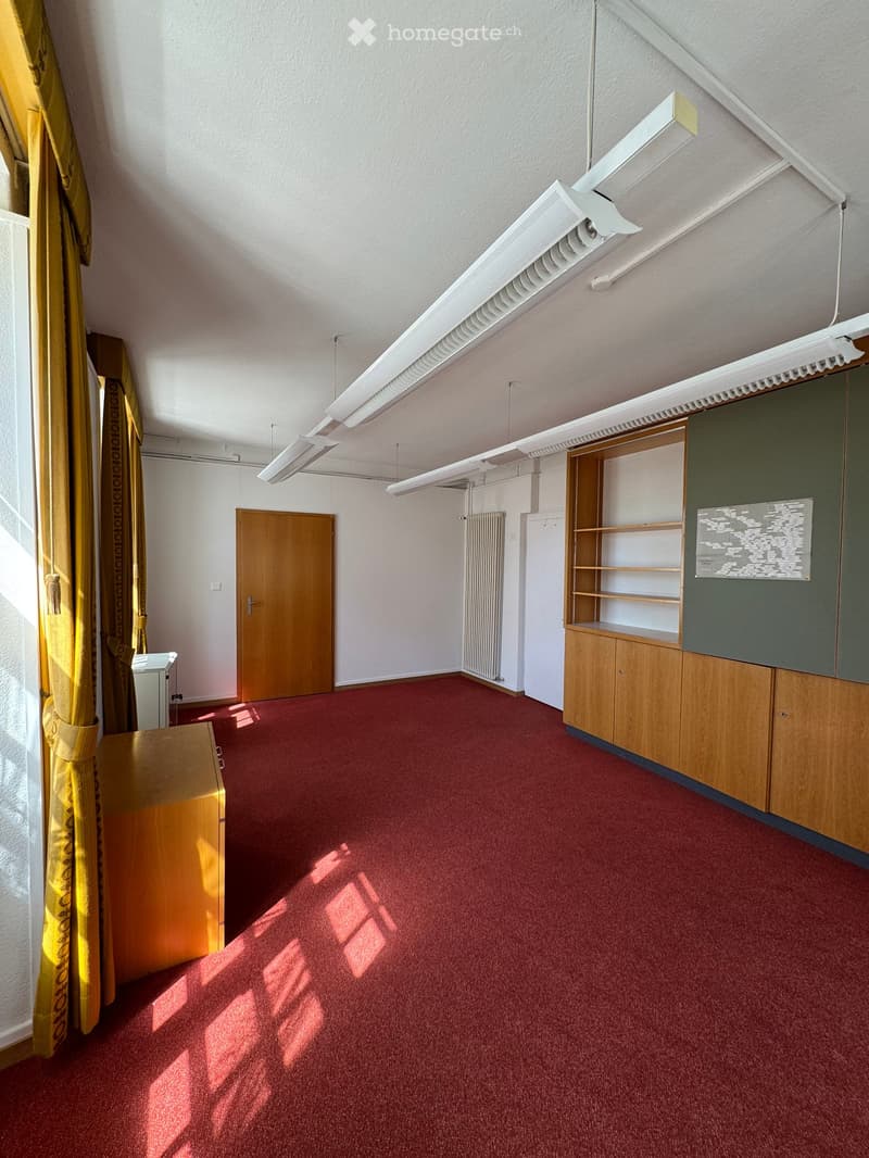 Empty room with red carpet, wooden door, built-in wooden shelving unit, radiator, and yellow curtains on the window.