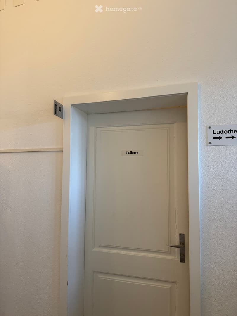 A hallway with a white door labeled 'Toilette' and a sign indicating directions to 'Ludotheque'.