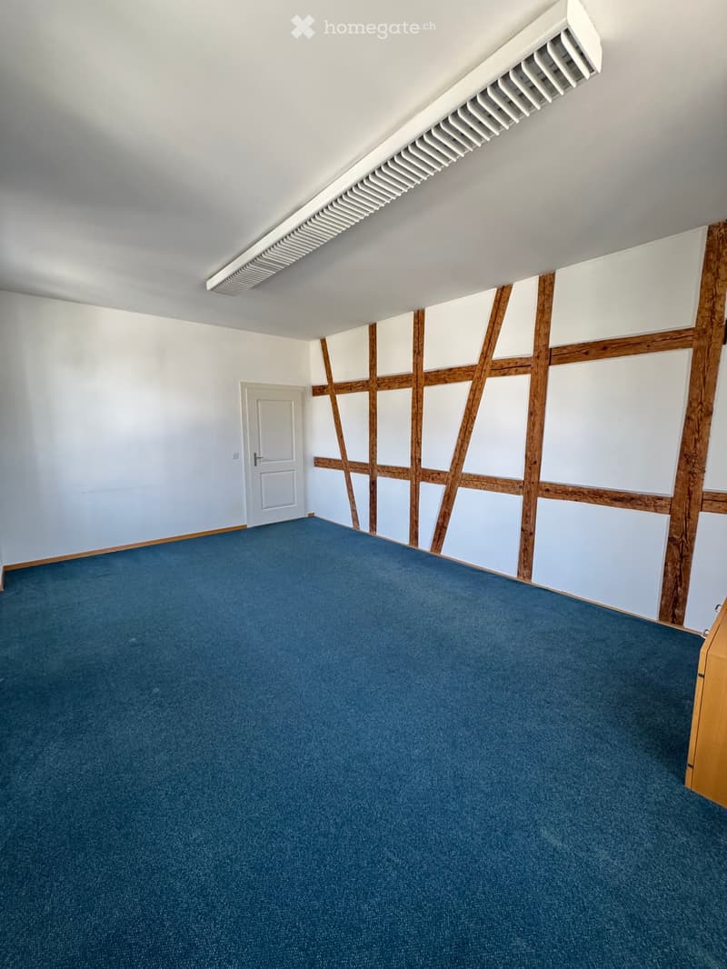 Empty room with blue carpet, white walls, wooden paneling, and a white door.