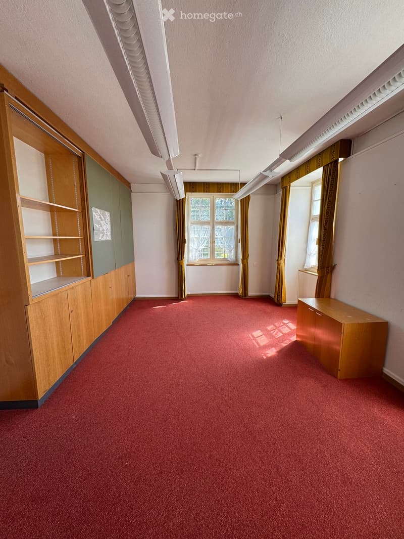 Empty room with red carpet, wooden cabinetry, and large windows with yellow curtains.
