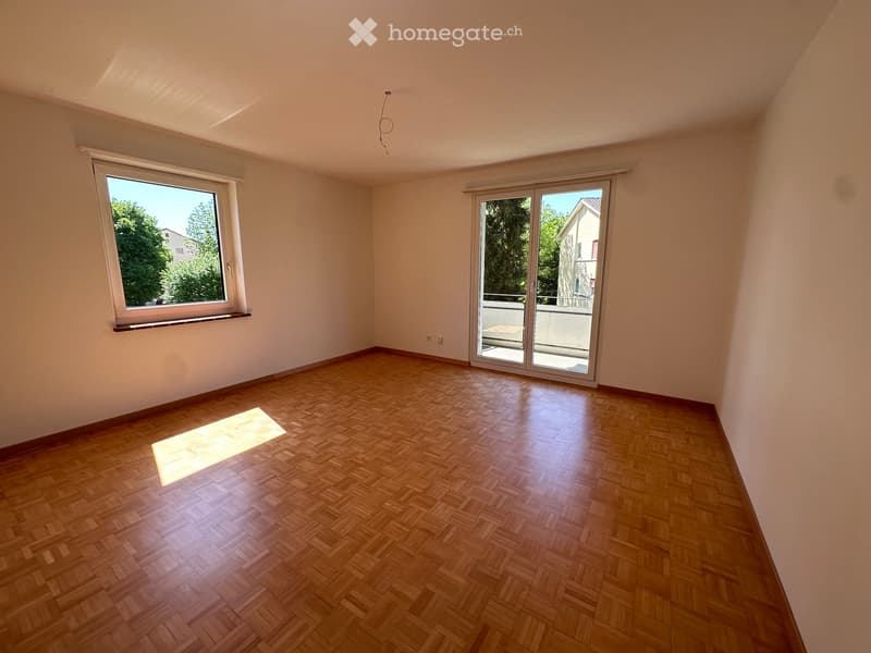 Empty room with wooden parquet flooring, large window, and sliding glass door leading to a balcony.
