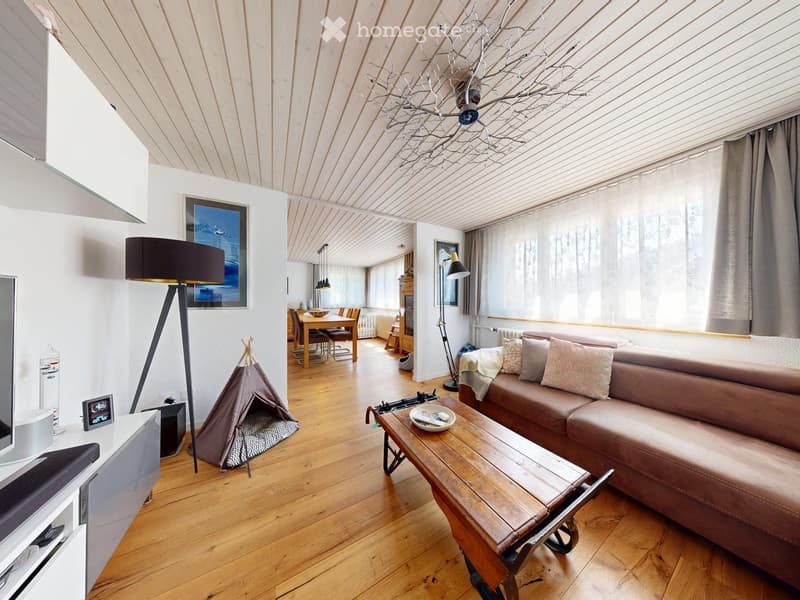 Open-plan living and dining area with wooden flooring, a brown leather sofa, a wooden coffee table, a floor lamp, a dining table with chairs, and a small teepee tent.