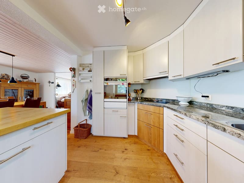 Bright, modern kitchen with white cabinets, wooden countertops, and a central island. Features include a sink, oven, and various kitchen utensils.