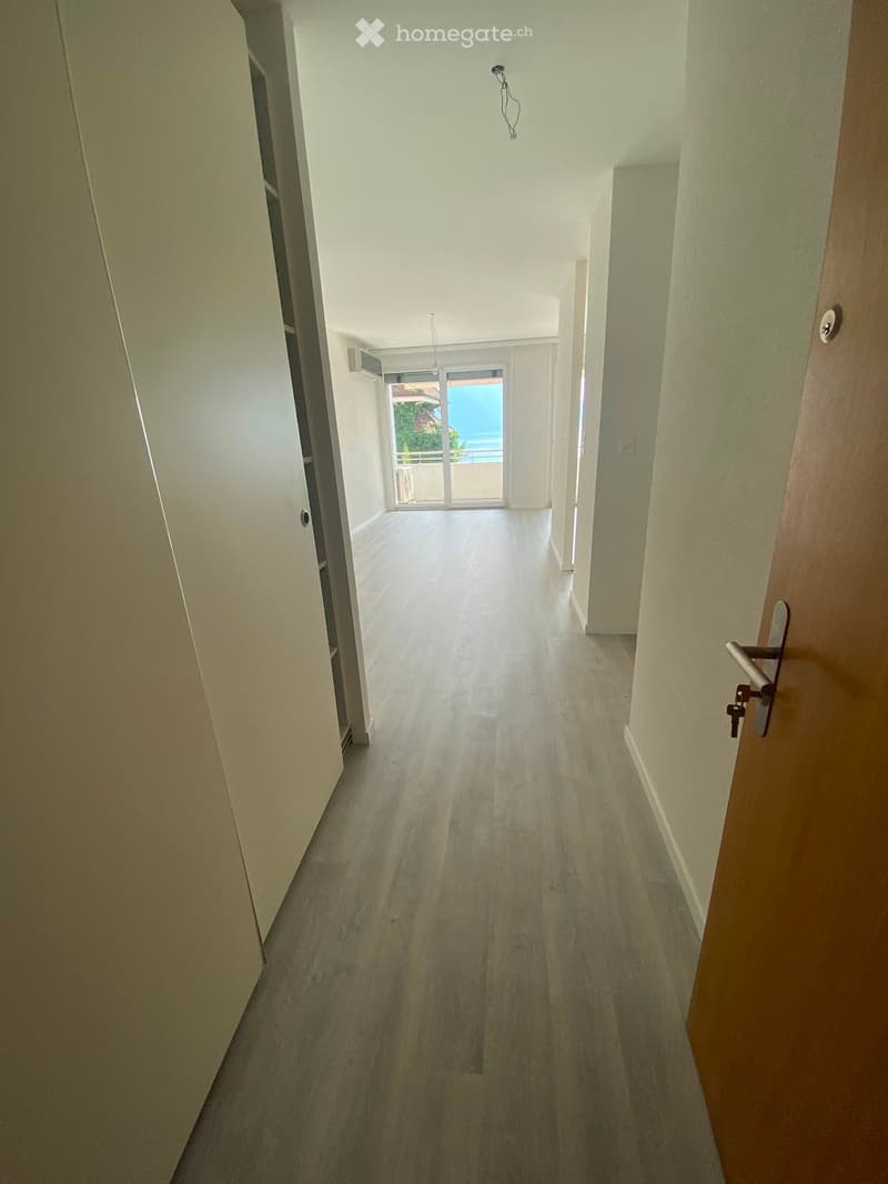 Empty hallway with light wooden flooring, white walls, and a sliding glass door leading to a balcony with a view of the sea.