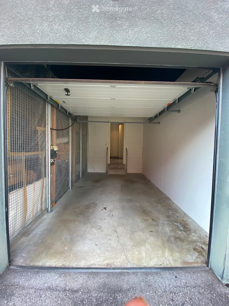 Empty, concrete-floored corridor with a gated area on the left and a doorway leading to another room at the end.