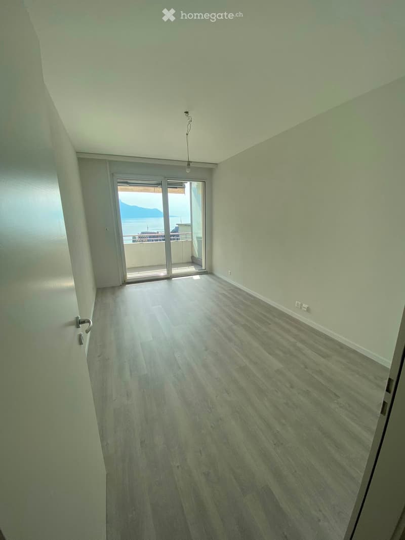Empty room with light-colored wooden flooring, white walls, and a sliding glass door leading to a balcony with a sea view.
