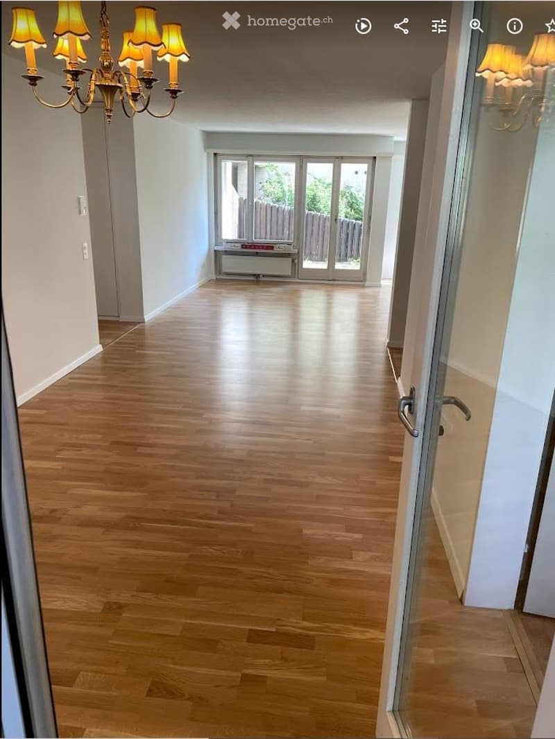 Empty hallway with wooden flooring, white walls, and a large sliding glass door leading to an outdoor area.