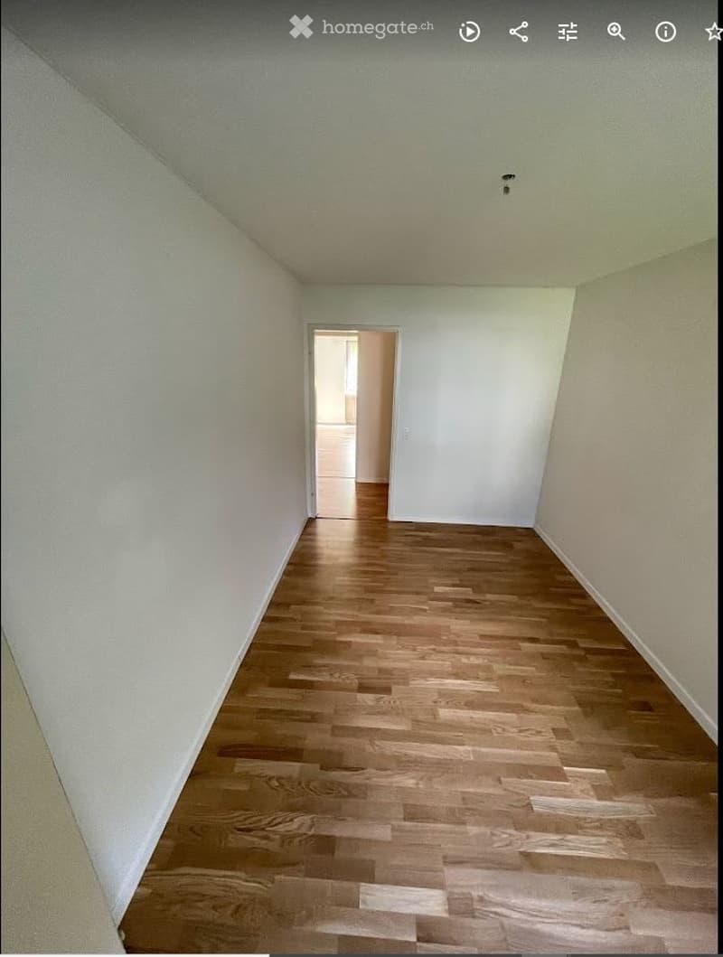 Empty room with light-colored walls and wooden flooring, featuring a doorway leading to another space.