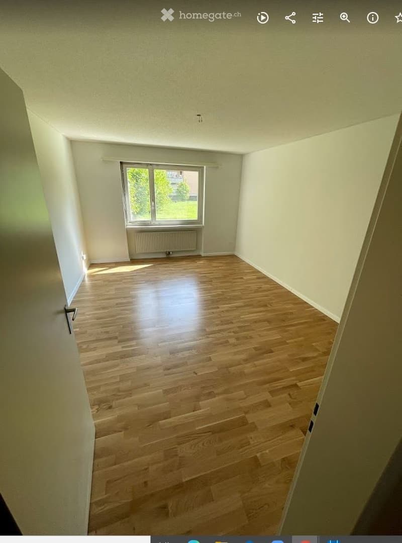 Completely empty room with wooden flooring, white walls, and a single window with a radiator below it.