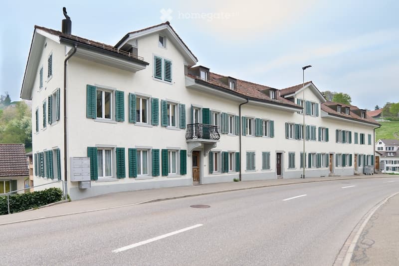 white exterior, green shutters, brown roof, balcony, street facing, multiple windows, mail slots
