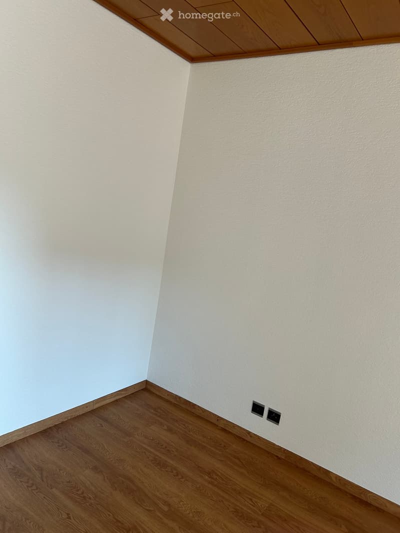 Empty room with light-colored walls, wooden floor, and electrical outlets visible on the wall.