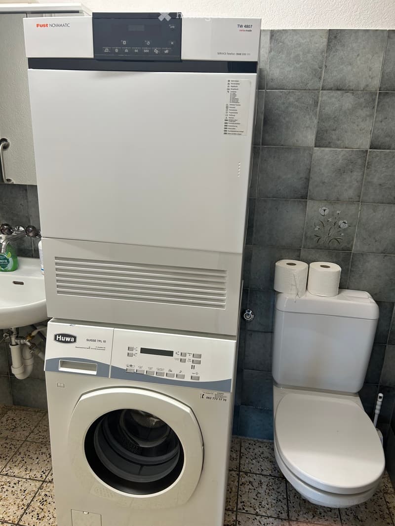Bathroom with a washing machine, toilet, toilet paper, and a sink.