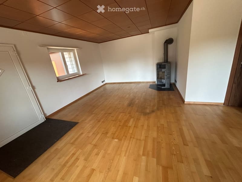 Empty room with wooden flooring, white walls, and a small window. A fireplace is present in the corner.