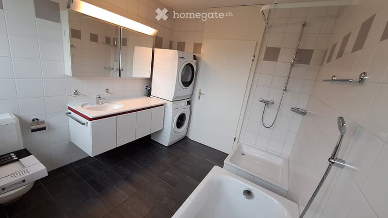 Modern bathroom with white tiles, a sink, a washing machine, a toilet, a bathtub, and a shower area.