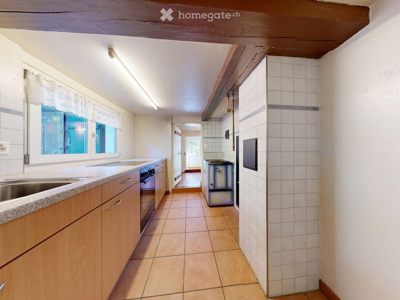 Modern kitchen with light wooden cabinets, granite countertop, stainless steel sink, and built-in oven. The space features tiled flooring and white tiled walls in the adjacent area.