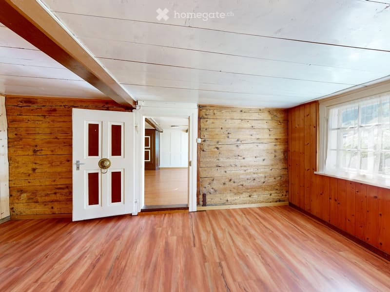 Empty room with wooden walls, polished wooden floor, white door with glass panels, and visible ceiling beams.