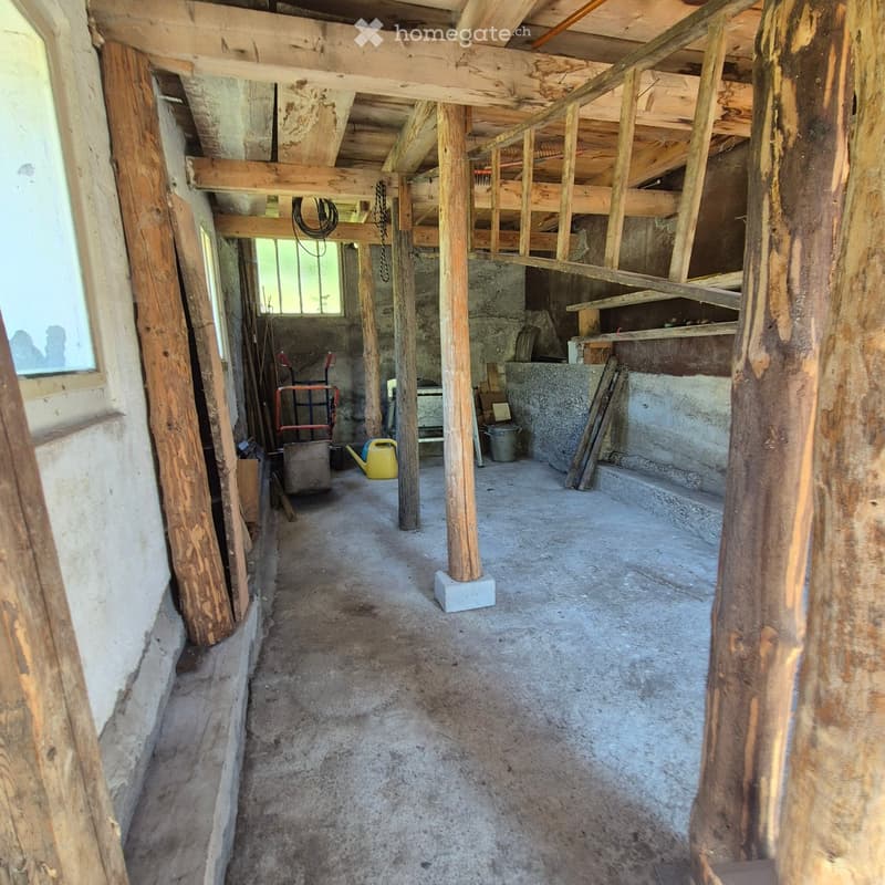 Empty room with exposed wooden beams and concrete floor, featuring wooden pillars and scattered tools and equipment.