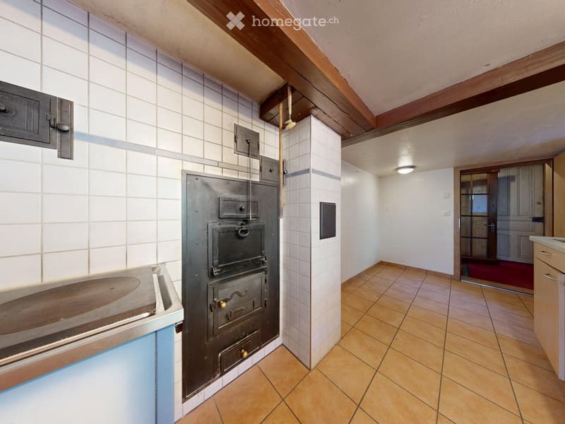 Kitchen with tiled walls, wooden ceiling beams, and a large stainless steel oven. The floor is tiled, and there is a sink visible on the left side.