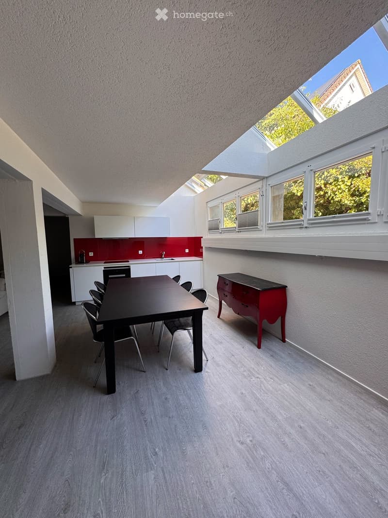 Bright, modern kitchen with white cabinets, red backsplash, and large windows. Includes a dining table with chairs, a red dresser, and a sink with a faucet.