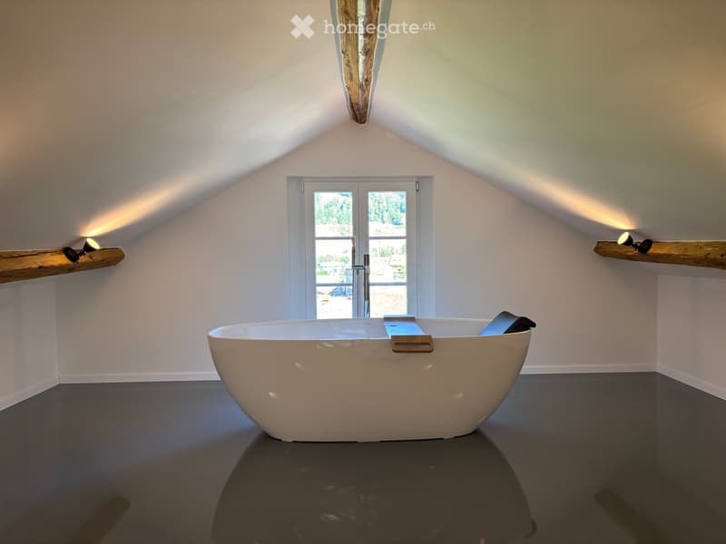 Modern bathroom with a large freestanding bathtub, sleek faucet, and wooden shelves with spotlights, featuring a skylight and large window offering a view.
