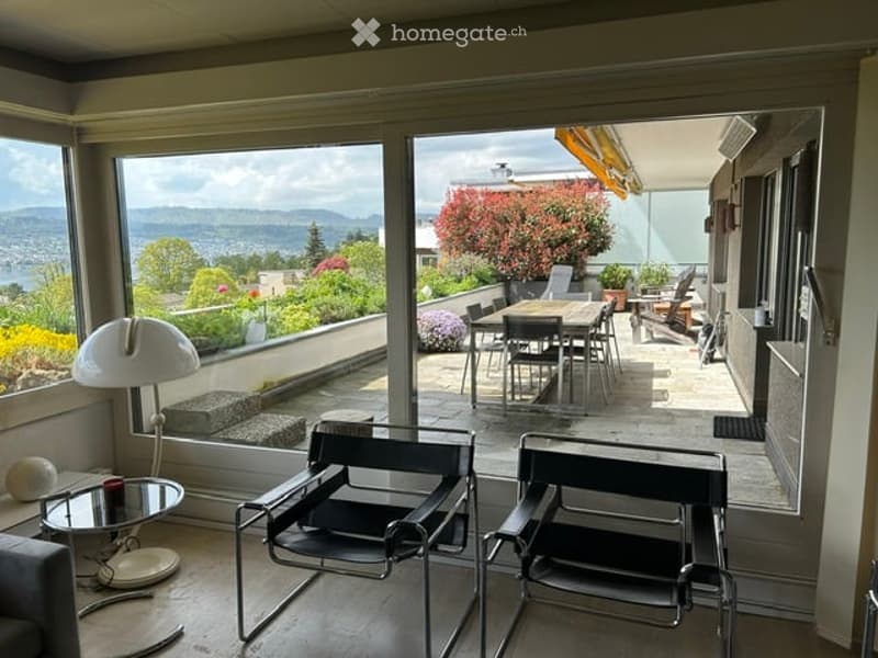 Bright living room with large windows offering a scenic mountain view, furnished with a sofa, a small table, and two modern chairs.