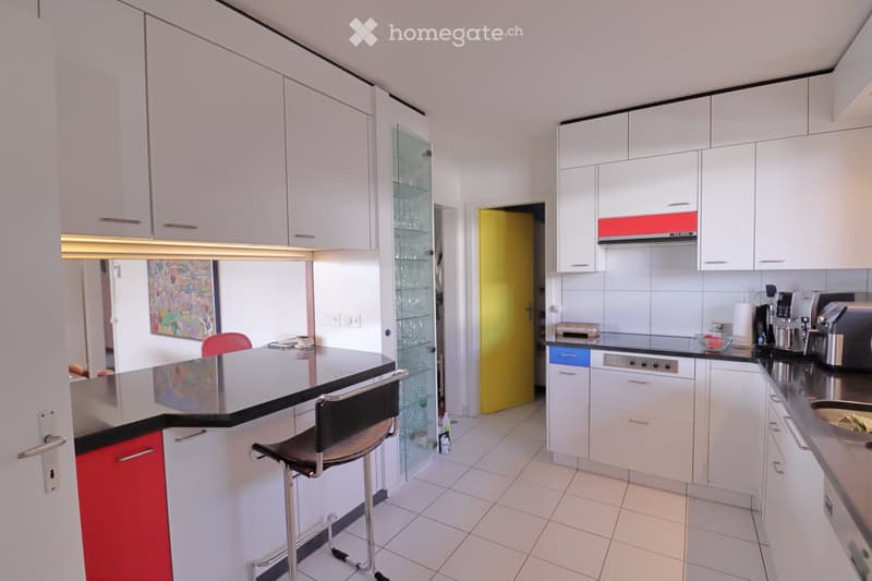 Modern kitchen with white cabinets, black countertops, and stainless steel appliances. Features a central island with bar stools, a coffee maker, and a sink.