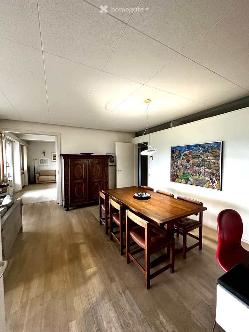 Dining area with a wooden dining table, chairs, a sofa, a cabinet, and a painting on the wall.