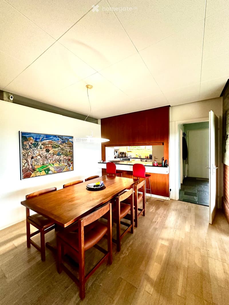 Dining area with a wooden dining table and chairs, a kitchen counter with stools, and a painting on the wall.