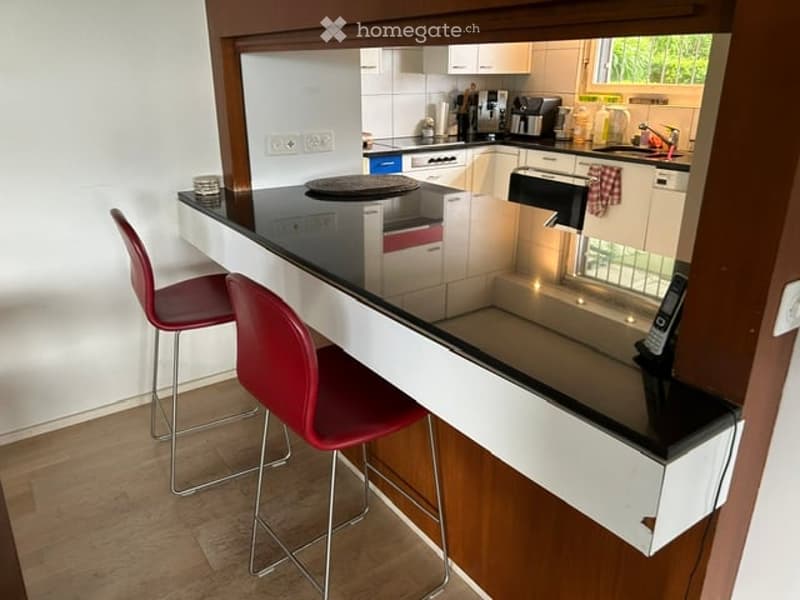 Modern kitchen with white cabinets, black countertop, red bar stools, and various appliances including a coffee maker and dishwasher.