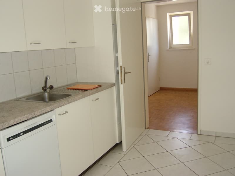 Modern kitchen with white cabinets, tiled walls, granite countertop, and a stainless steel sink. A dishwasher is installed under the countertop, and a small orange tray sits on the counter.