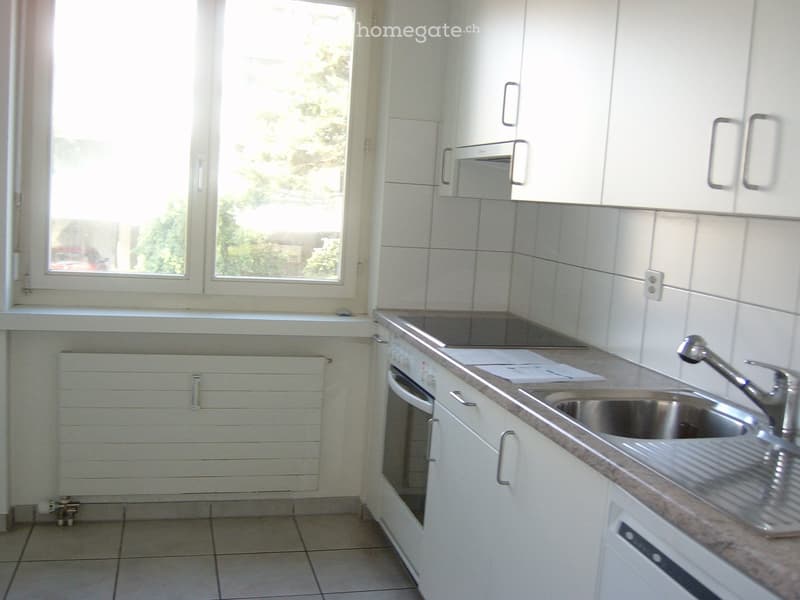 Modern kitchen with white cabinets, tiled walls, and a stainless steel sink with a faucet. The space includes an oven and a window letting in natural light.