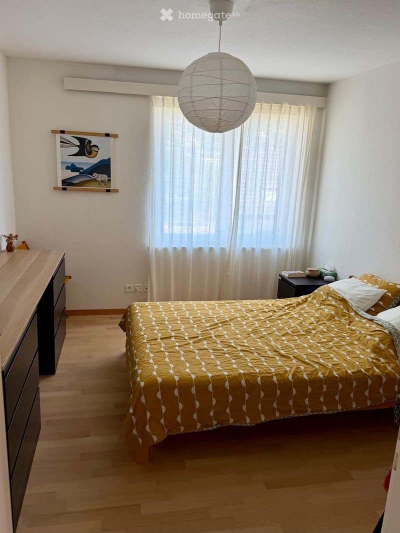 Cozy bedroom with wooden flooring, a double bed with yellow bedding, a nightstand, a dresser, and a hanging paper lantern light fixture.