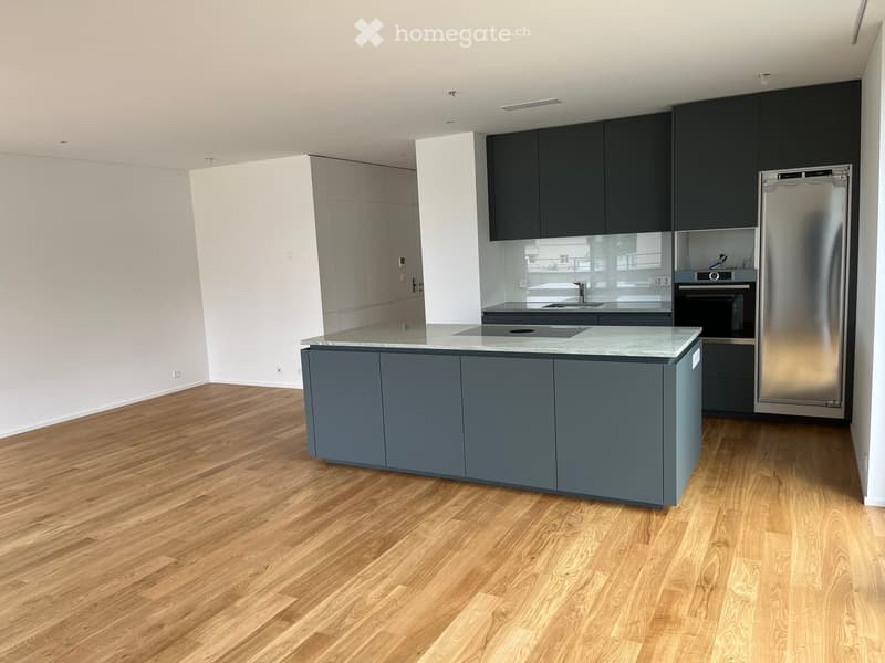Modern kitchen with a central island, dark grey cabinets, stainless steel appliances, and light wooden flooring.