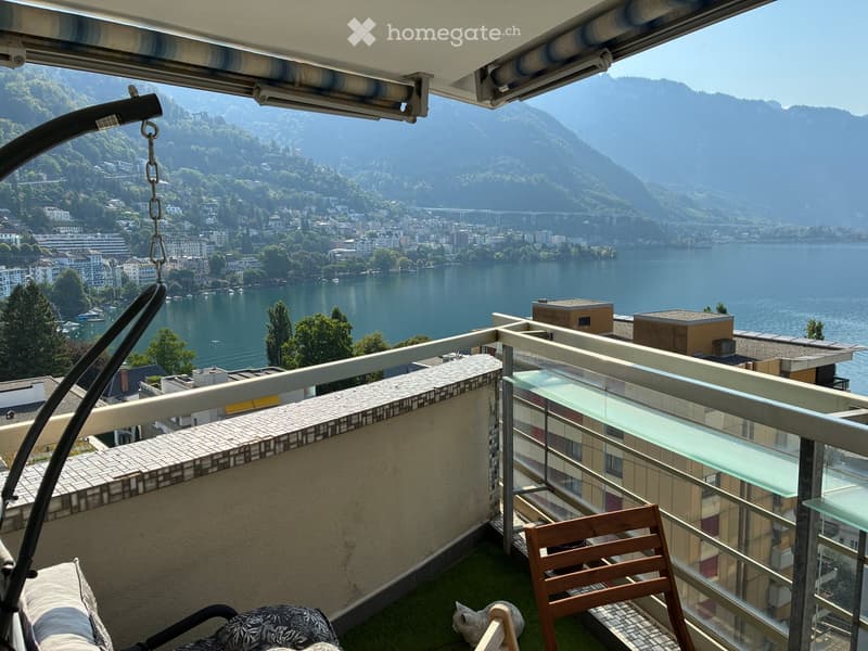 Balcony with a scenic view of a lake and mountains, featuring a wooden chair, a small table, and a hanging chair.