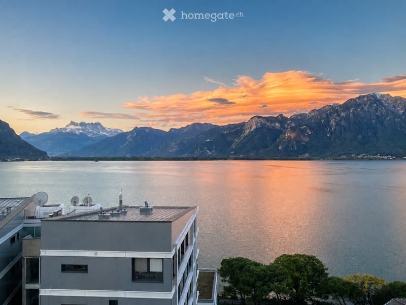 Modern building with a panoramic view of a lake and mountain range at sunset.