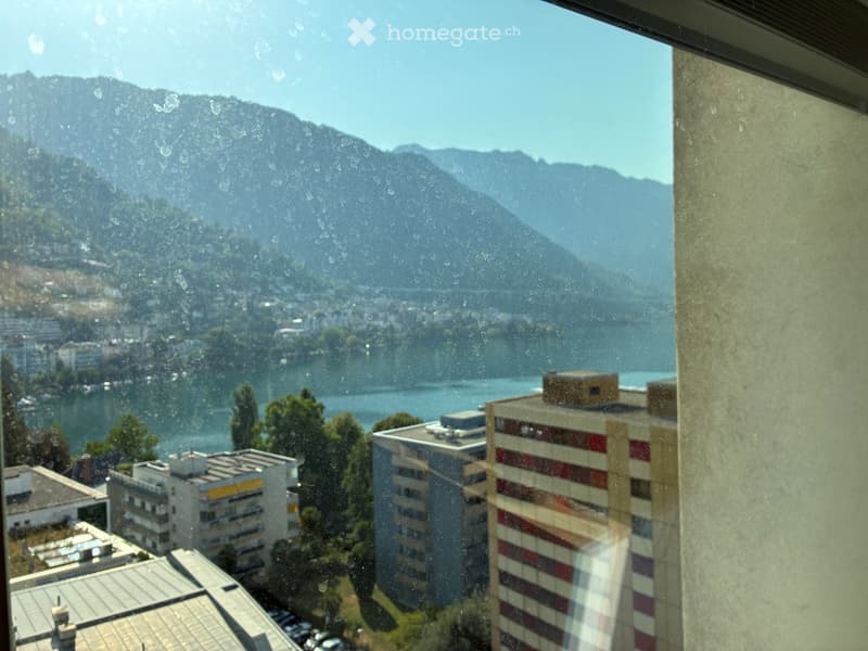 View from a balcony showing a lake, mountains, and surrounding buildings.