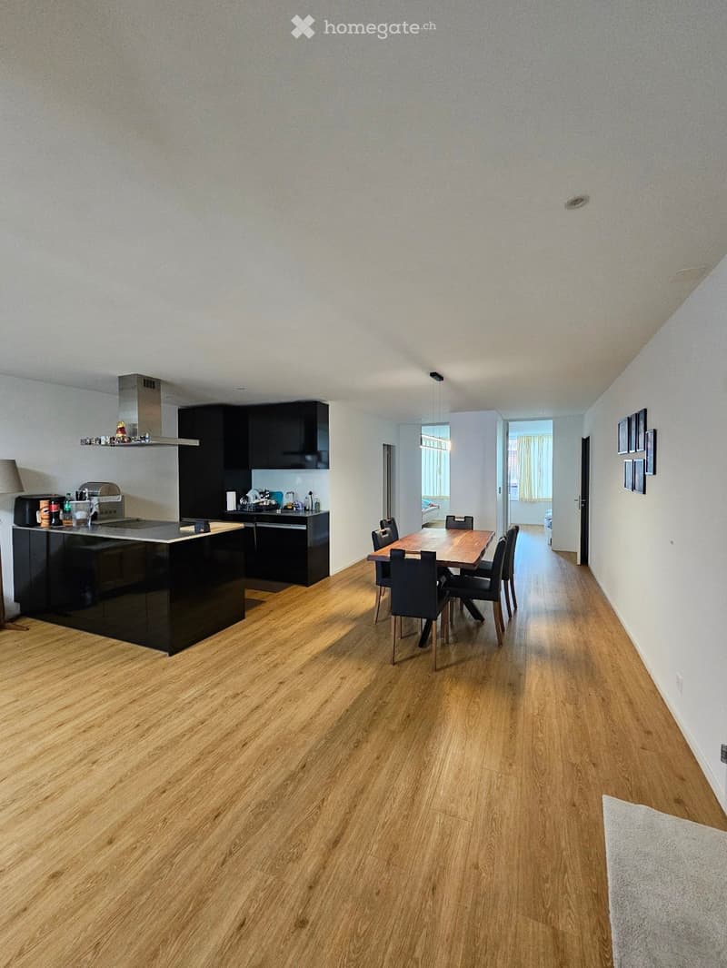 Open-plan kitchen and dining area with wooden flooring, black kitchen island, dining table with chairs, and modern cabinets.