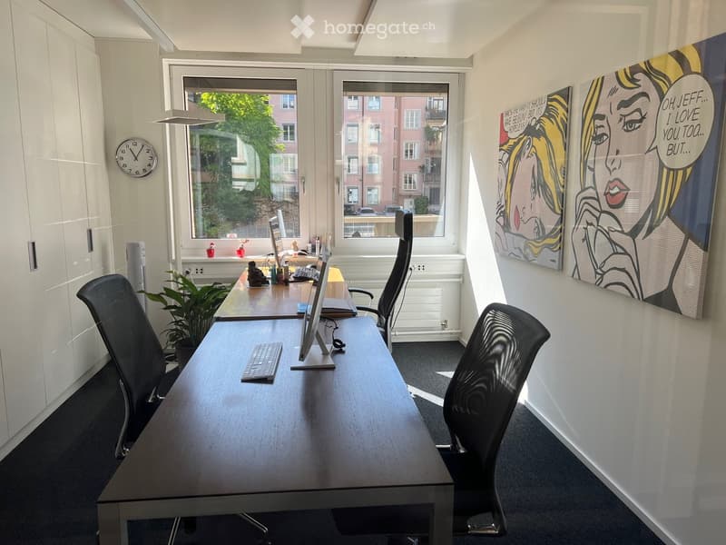 Office room with two desks, two black chairs, two computer monitors, keyboard, mouse, clock, two paintings, potted plant, radiator