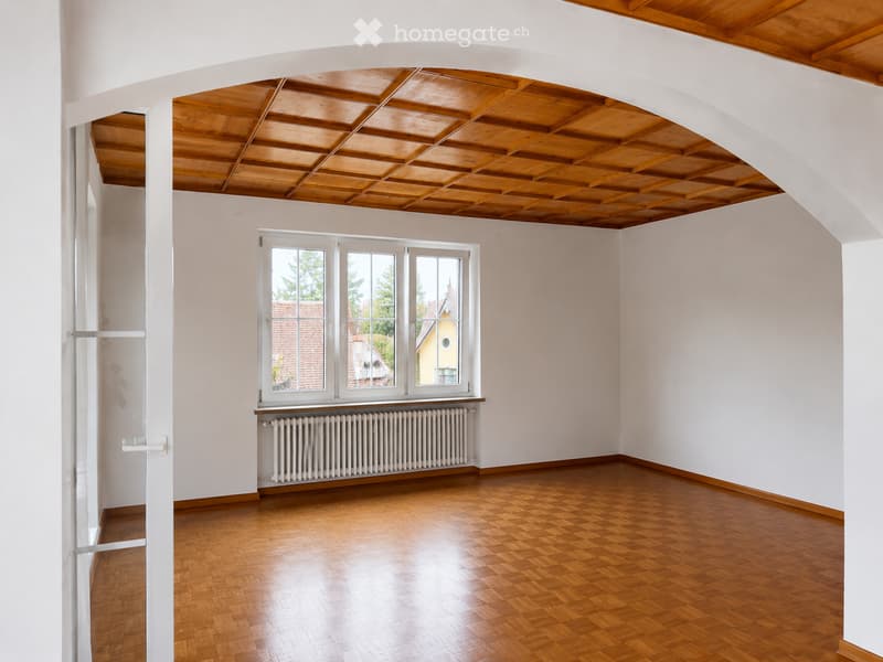 Empty room with wooden parquet flooring, white walls, large windows, and a radiator below the windows.