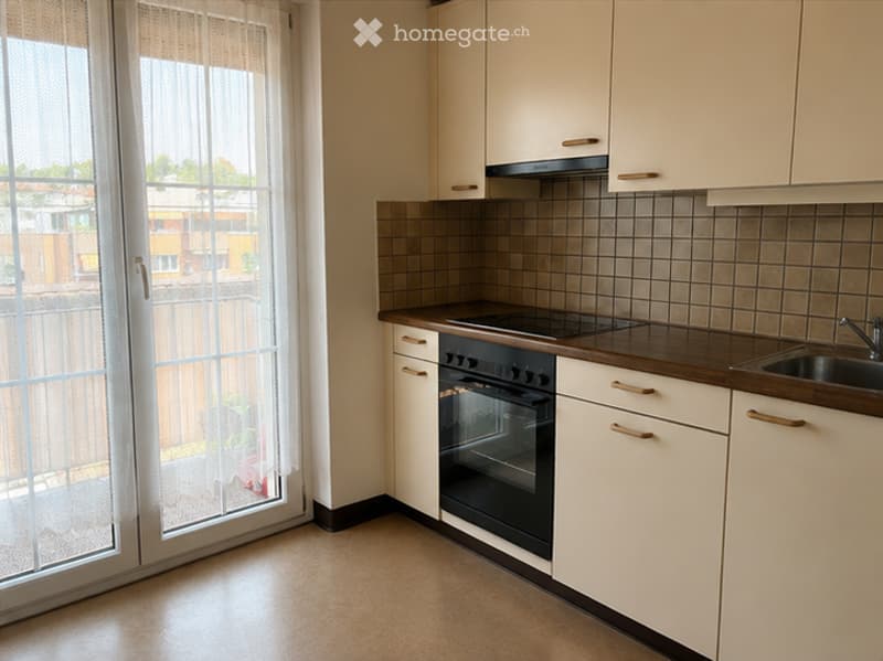 Modern kitchen with white cabinets, dark countertops, and a built-in oven. Features a large window with blinds and a sliding glass door leading outside.