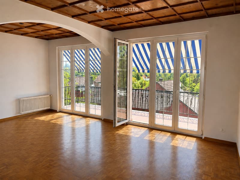 Empty room with wooden flooring, white walls, large glass doors with blue and white striped blinds leading to a balcony, and a radiator on the left wall.