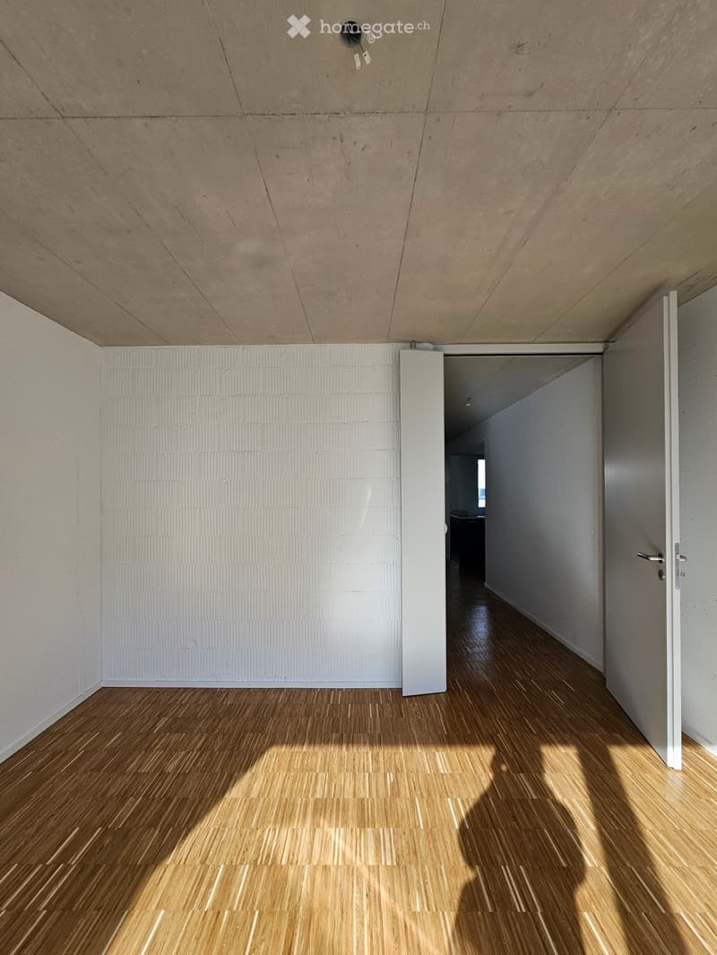 Empty hallway with wooden flooring and white walls, featuring a partially open door leading to another room.