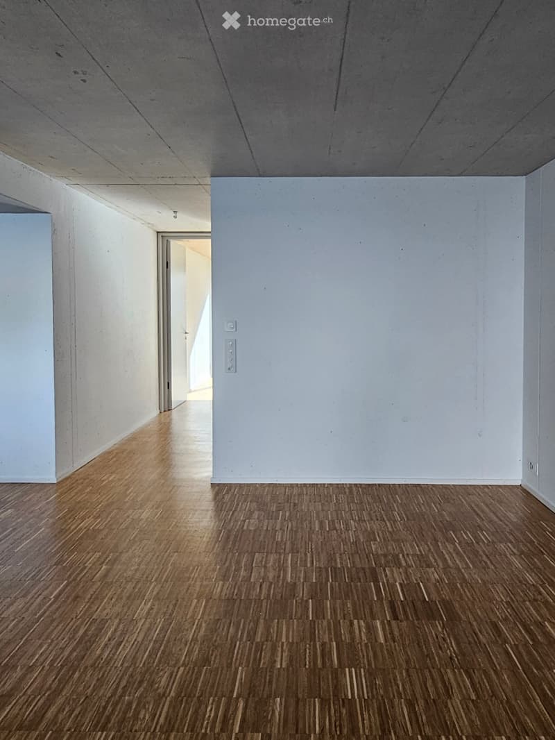 Empty hallway with wooden flooring and white walls, featuring a door at the end and electrical outlets on the wall.