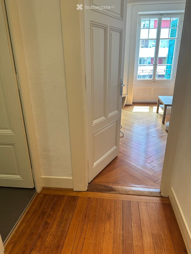 Wooden floor hallway with a door leading to a room with a small table and a window with a view of a balcony.