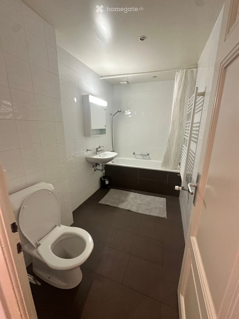 Modern bathroom with white tiles, a toilet, a sink, a bathtub, a shower, and a mirror cabinet.