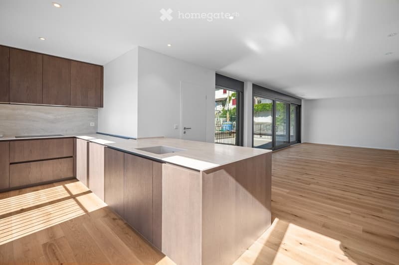 Modern kitchen with light wood cabinets, a central island, and large windows leading to an outdoor area.